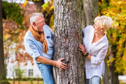 Senior und Seniorin stehen in einem park an einem Baumstamm